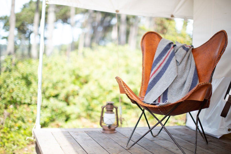 Luxury glamping tent nestled among towering redwoods at Mendocino Grove, featuring a private deck and cozy outdoor seating area