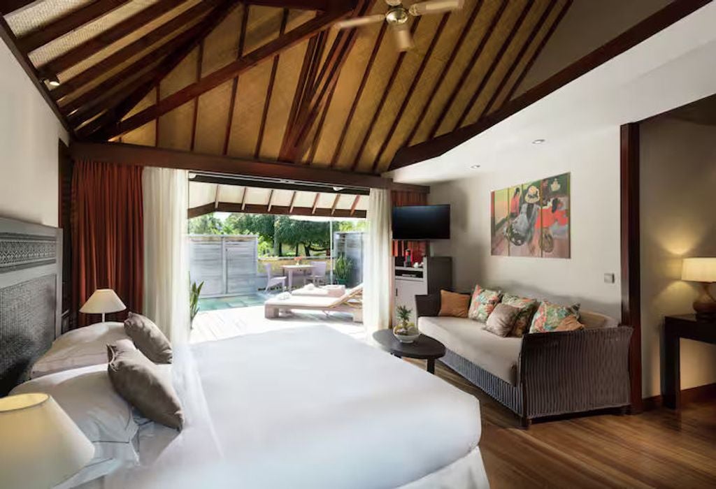 Luxurious king bed room with vaulted wood ceiling, sliding glass doors, plush white bedding, and tropical garden views in Moorea