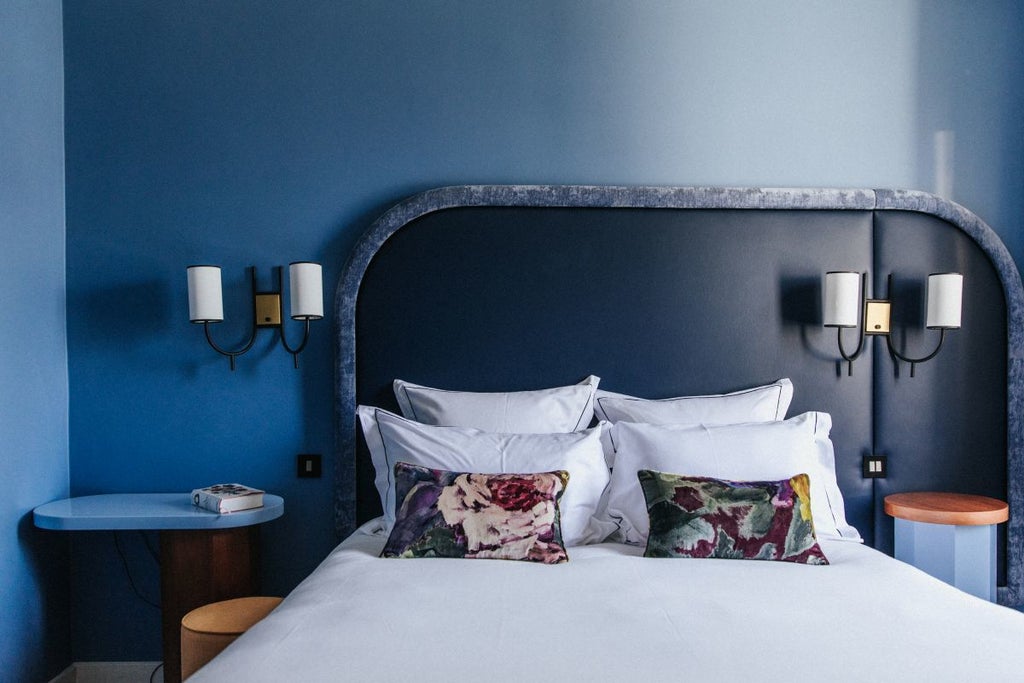 Chic Parisian single room with soft neutral tones, plush white bedding, elegant vintage-style furniture, and soft natural lighting from large windows.