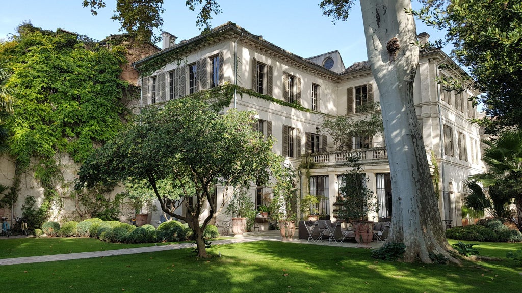 Elegant French boutique hotel exterior with ornate facade, wrought-iron balconies, and lush garden, showcasing refined luxury in historic architecture