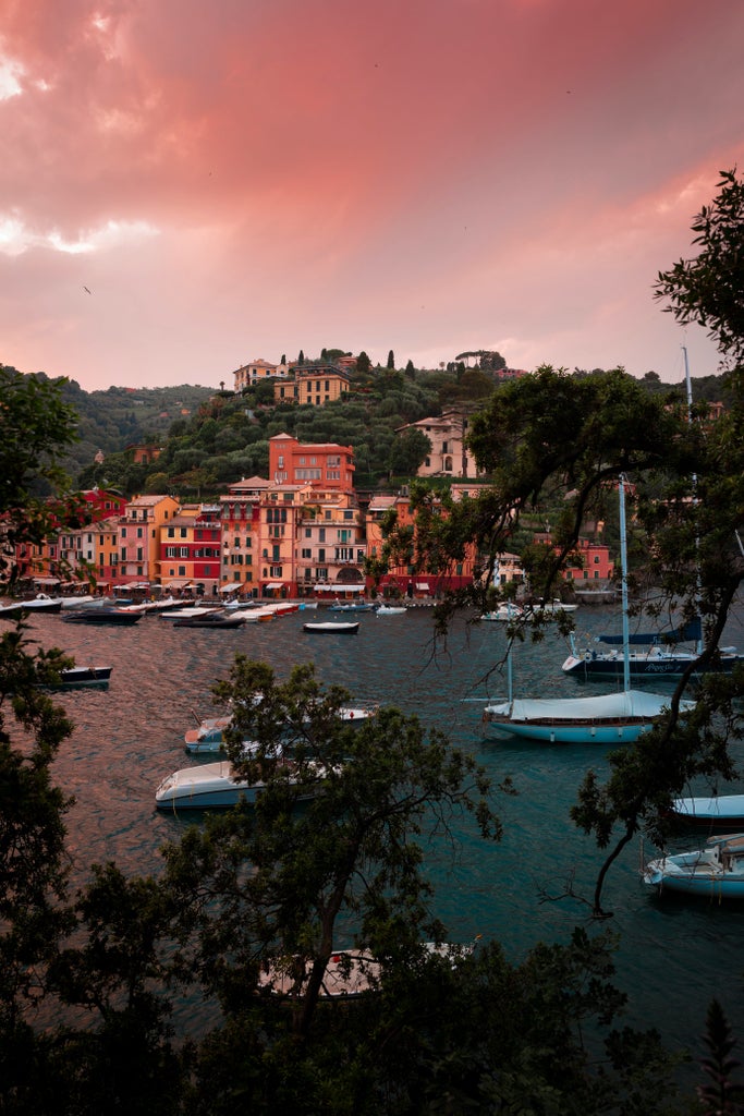 Colorful pastel buildings with luxury yachts line the crystal-clear waters of Portofino's harbor, nestled against lush Mediterranean hillside