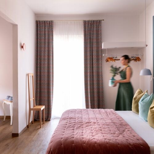 Elegant junior suite with soft cream walls, plush white bedding, rich wooden furniture, and panoramic Tuscan countryside view through large windows