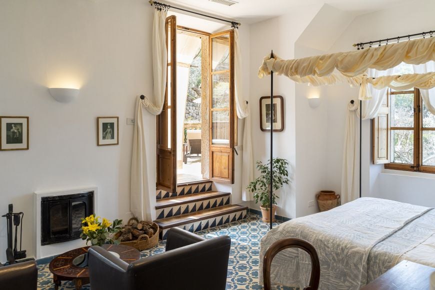 Elegant deluxe room at Ca's Xorc Luxury Retreat, featuring plush white bedding, rustic stone walls, and panoramic Mediterranean landscape view in Spain