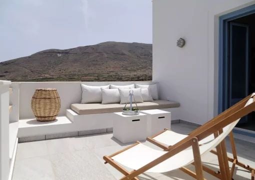 Elegant white stone villa with blue-trimmed windows overlooking Santorini's azure coastline, featuring a luxurious private terrace with traditional Greek architectural details