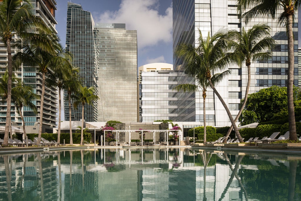 Oceanfront luxury hotel with sleek glass tower design, palm-lined infinity pool and private beach cabanas at sunset in Miami