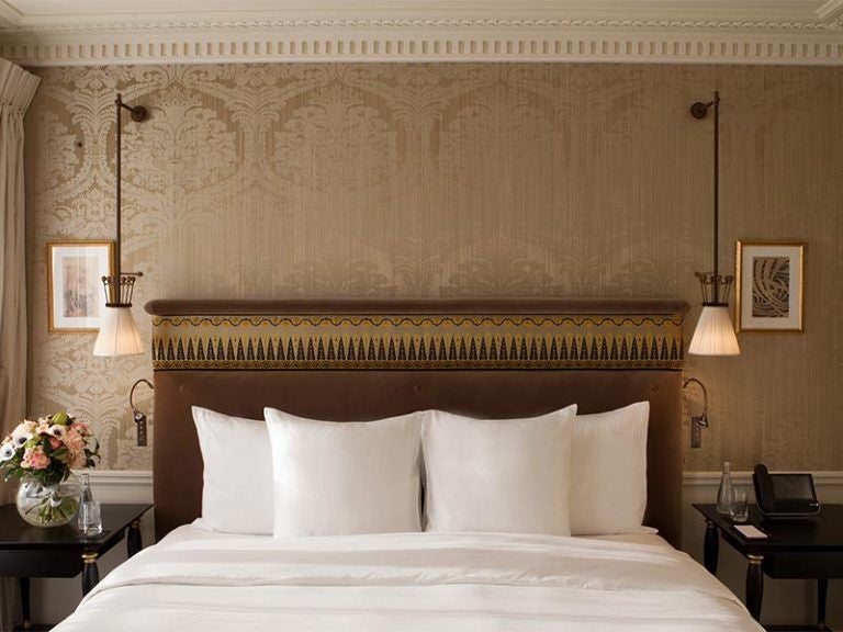 Opulent Parisian hotel room with silk-draped windows, antique furnishings, crystal chandelier, and plush king bed in cream and gold tones