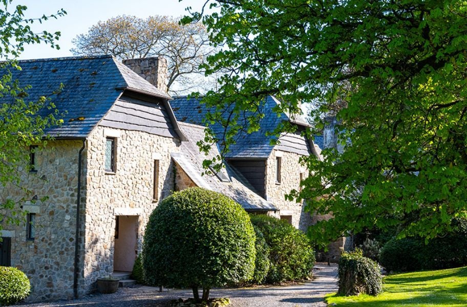 Elegant stone manor nestled in lush Devon countryside, Bovey Castle Hotel's grand facade blends historic architecture with verdant landscape and manicured grounds.