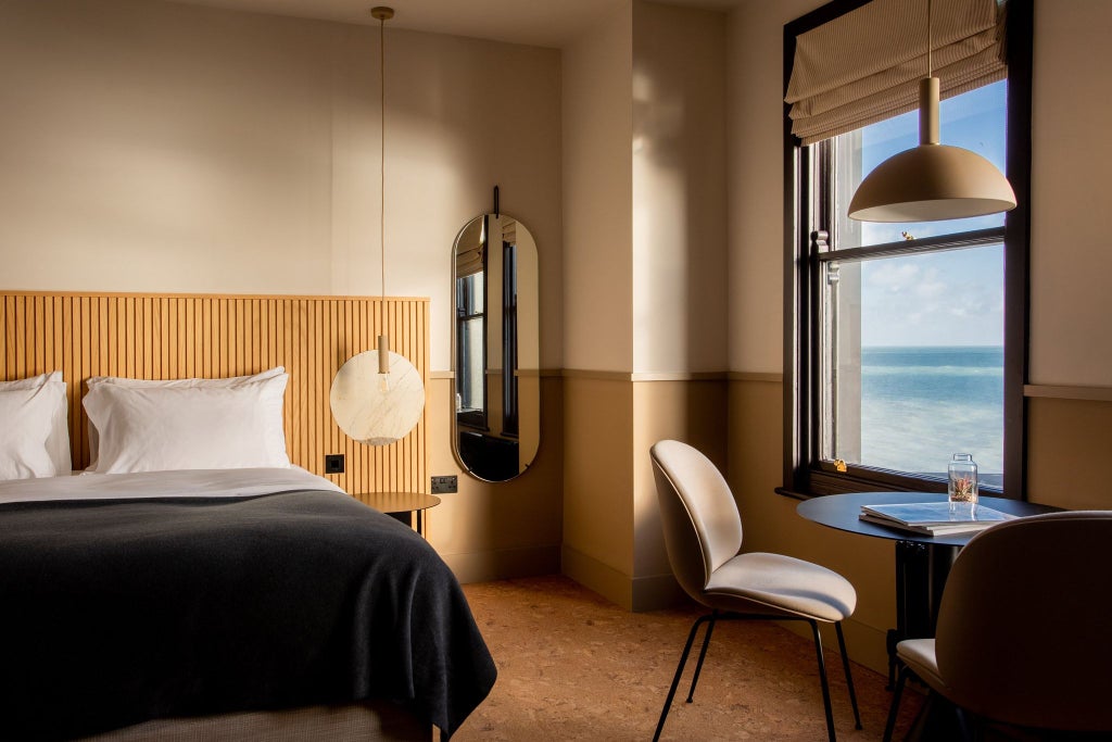 Spacious sea view hotel room with contemporary design, plush white bedding, large windows overlooking coastal scenery, and elegant freestanding bathtub