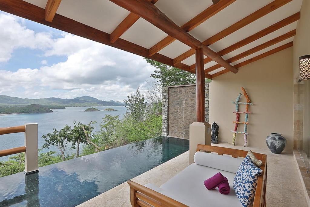 Luxurious infinity pool overlooking lush Costa Rican jungle and Pacific Ocean at sunset, with modern lounge chairs and parasols