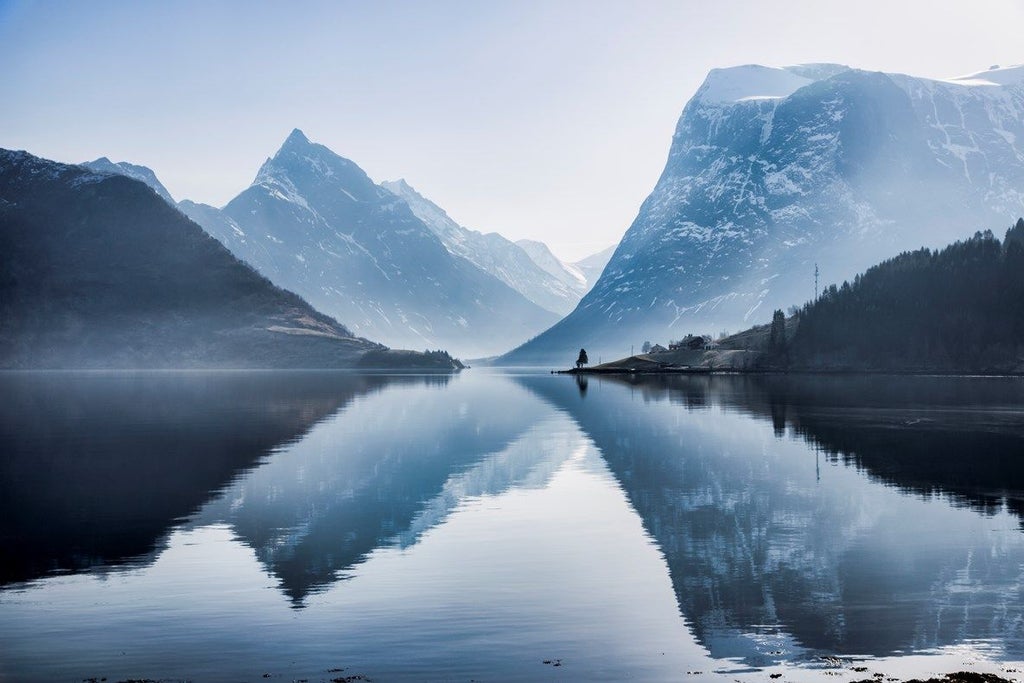 Luxurious wooden yacht cruising through narrow Norwegian fjord, surrounded by towering cliffs and pristine emerald waters