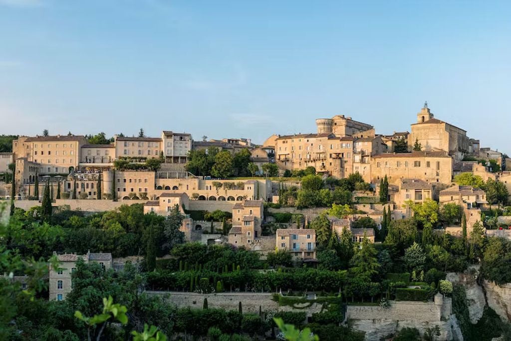 Five-star stone palazzo perched on cliff edge in Provence, with elegant terraced gardens and panoramic views of Luberon valley at sunset