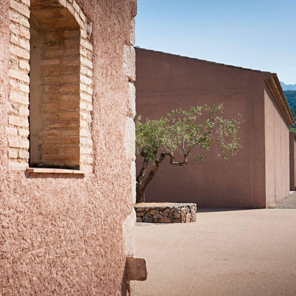 Luxurious Spanish winery hotel nestled among vineyards, featuring stone architecture, warm terracotta tones, and sweeping landscape views at sunset.