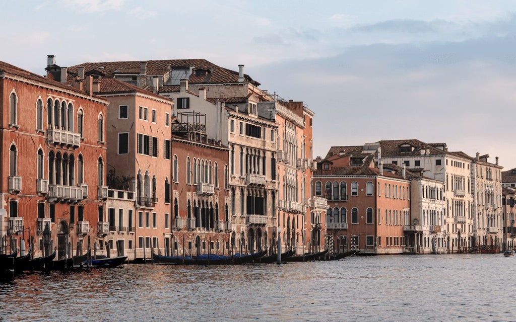 Elegant boutique hotel facade in Venice, with historic stone architecture, ornate balconies, and warm Mediterranean lighting at dusk