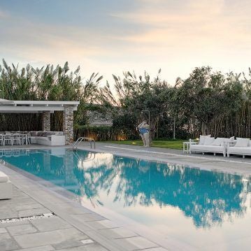 Luxurious whitewashed Cycladic hotel terrace overlooking azure Aegean Sea, with minimalist design and infinity pool at sunset