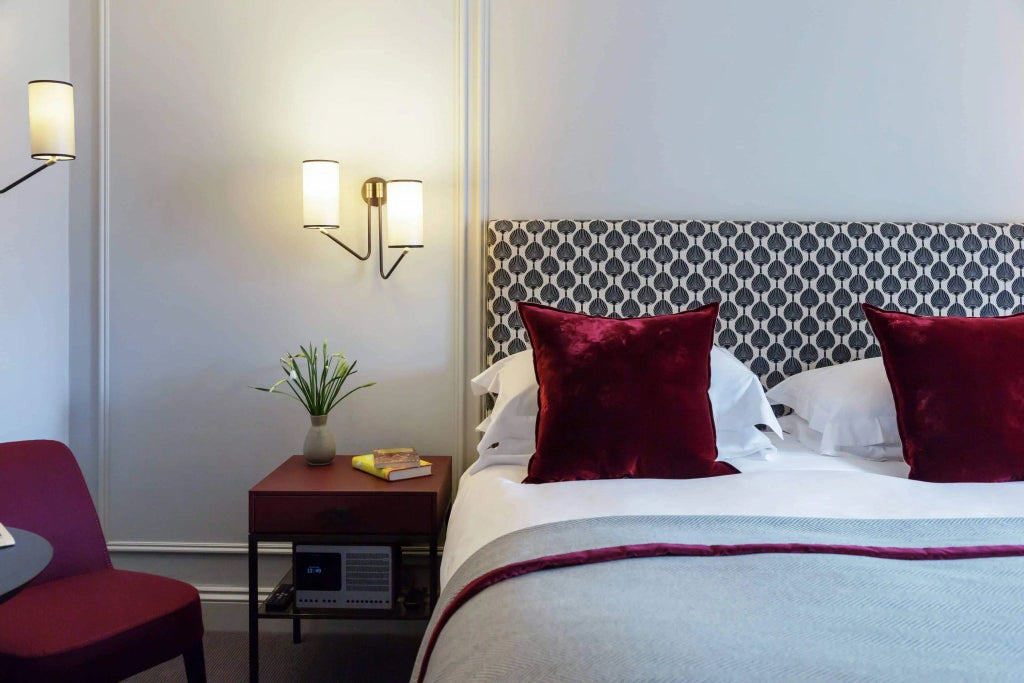 Classic hotel room with elegant four-poster bed, soft cream walls, antique wooden furniture, and large sash windows overlooking a serene British courtyard.