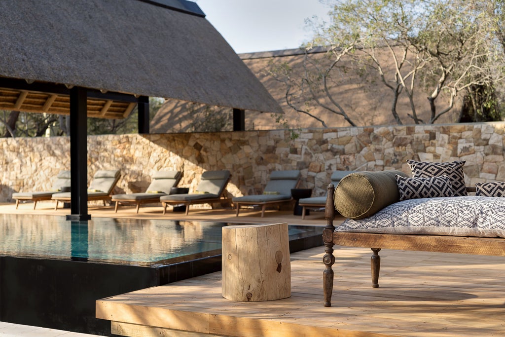 Elegant safari lodge with thatched roof and wooden deck overlooking a peaceful waterhole surrounded by African bushland at sunset