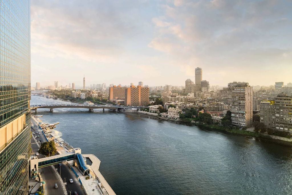 Grand twin towers of The St. Regis Cairo rise majestically along the Nile River, with ornate architecture and warm golden lighting at dusk