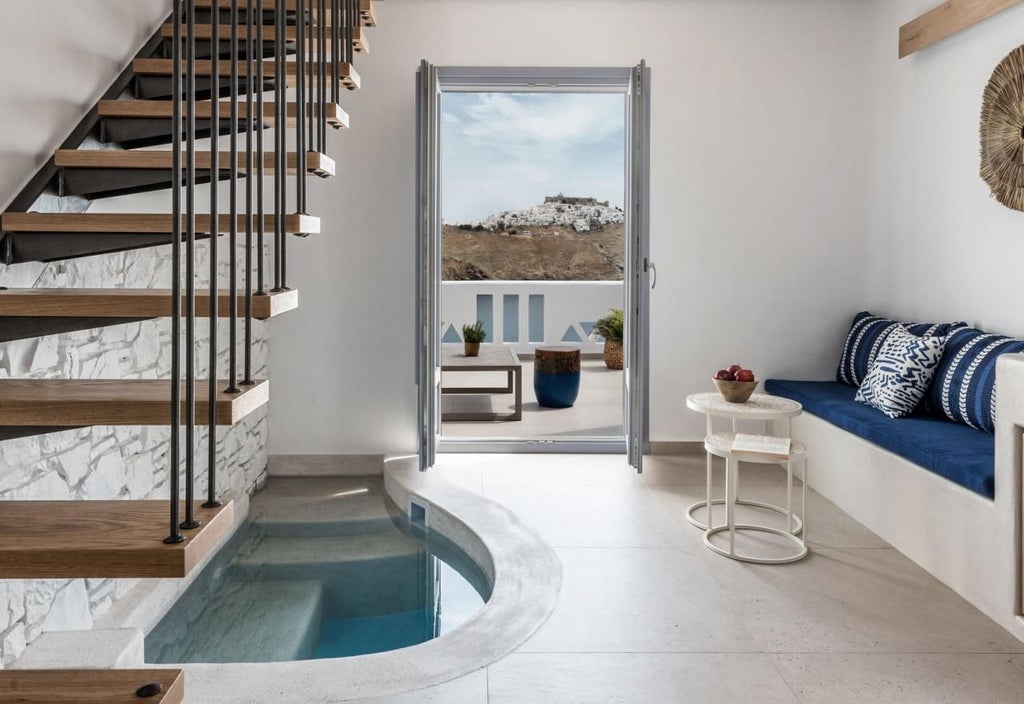 Elegant Aegean-style honeymoon suite with white-washed walls, minimalist decor, private balcony overlooking azure waters of Greek island landscape