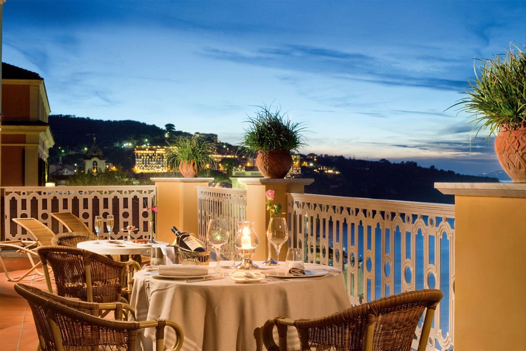 Elegant cliffside hotel with ornate Italian architecture, lush Mediterranean gardens and panoramic views over Sorrento Bay at sunset