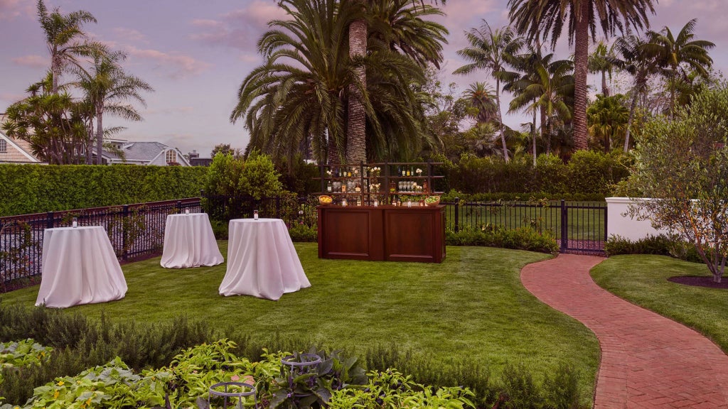 Luxurious oceanfront resort with pristine white buildings, palm trees, and elegant pool overlooking the azure waters of Miramar Beach, California.