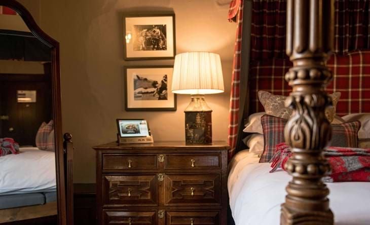 Luxurious Charles I Suite at historic Lygon Arms hotel, featuring elegant four-poster bed, ornate period furnishings, and rich wooden paneled walls in soft, warm tones