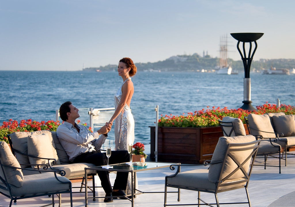 Grand Ottoman-style palace hotel with ornate white facade and lush gardens overlooking the Bosphorus strait in Istanbul at sunset