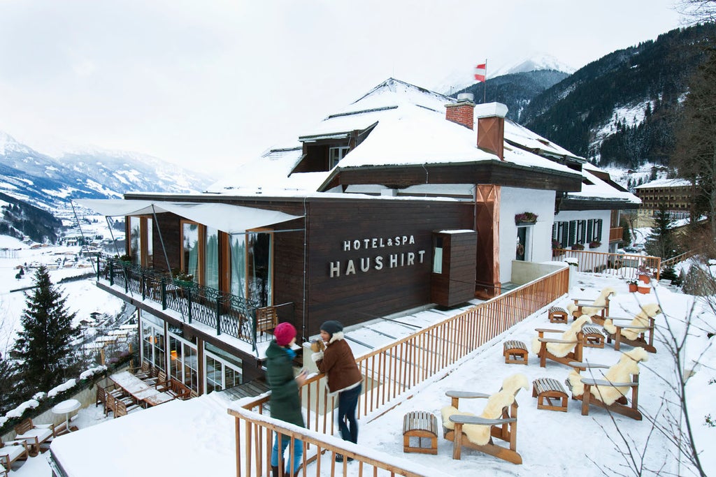 Elegant Tyrolean hotel nestled in Austrian Alps, featuring modern glass facade, wooden balconies and snow-capped mountain backdrop