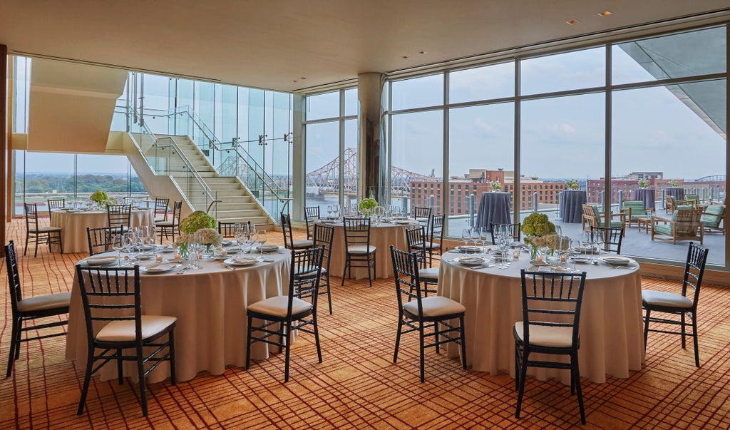 Modern luxury hotel exterior with glass facade, illuminated at dusk, reflecting city lights against St. Louis skyline and Gateway Arch