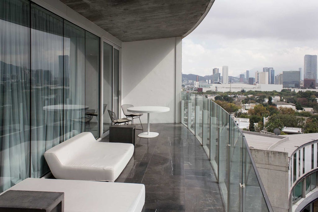 Modern glass-fronted luxury hotel with sleek architectural design, reflecting Monterrey's urban landscape, set against dramatic mountain backdrop at sunset