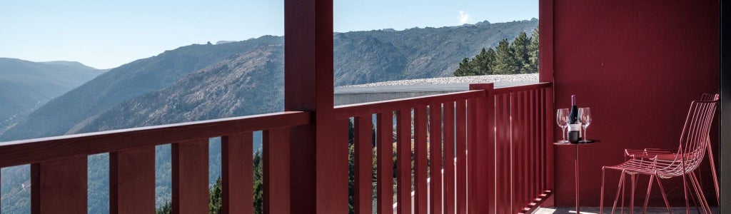 Elegant mountain-view hotel room with contemporary design, wooden accents, plush white bedding, and expansive windows overlooking scenic Portuguese landscape