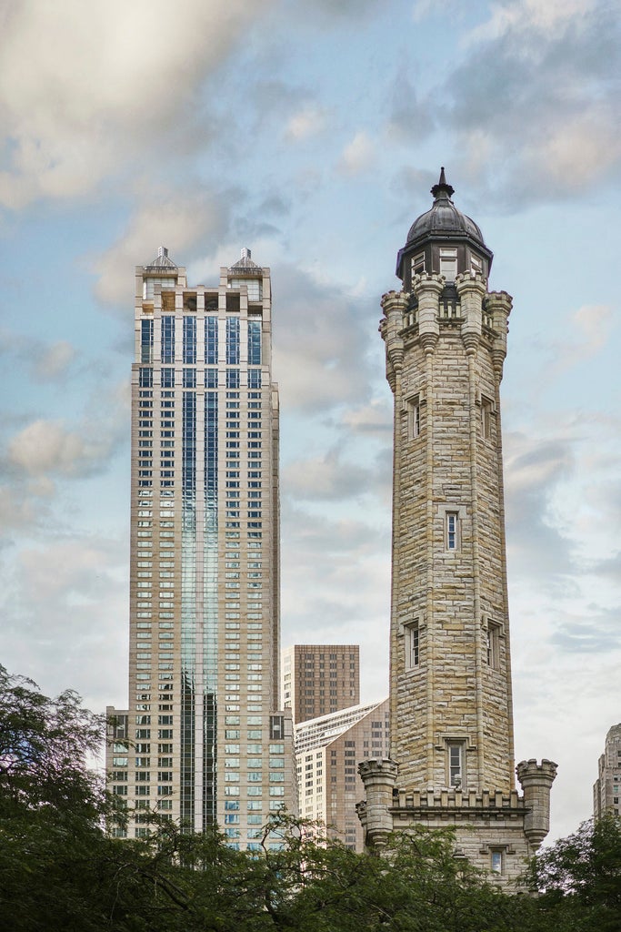 Modern skyscraper hotel with glass facade reflecting sunlight, elegant entrance with gold accents and lush seasonal landscaping in Chicago's Gold Coast