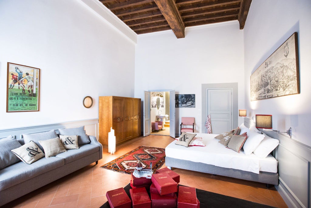 Elegant Tuscan-style deluxe room with ornate chandelier, antique wooden furnishings, and plush white linens against soft neutral walls in a boutique Italian hotel