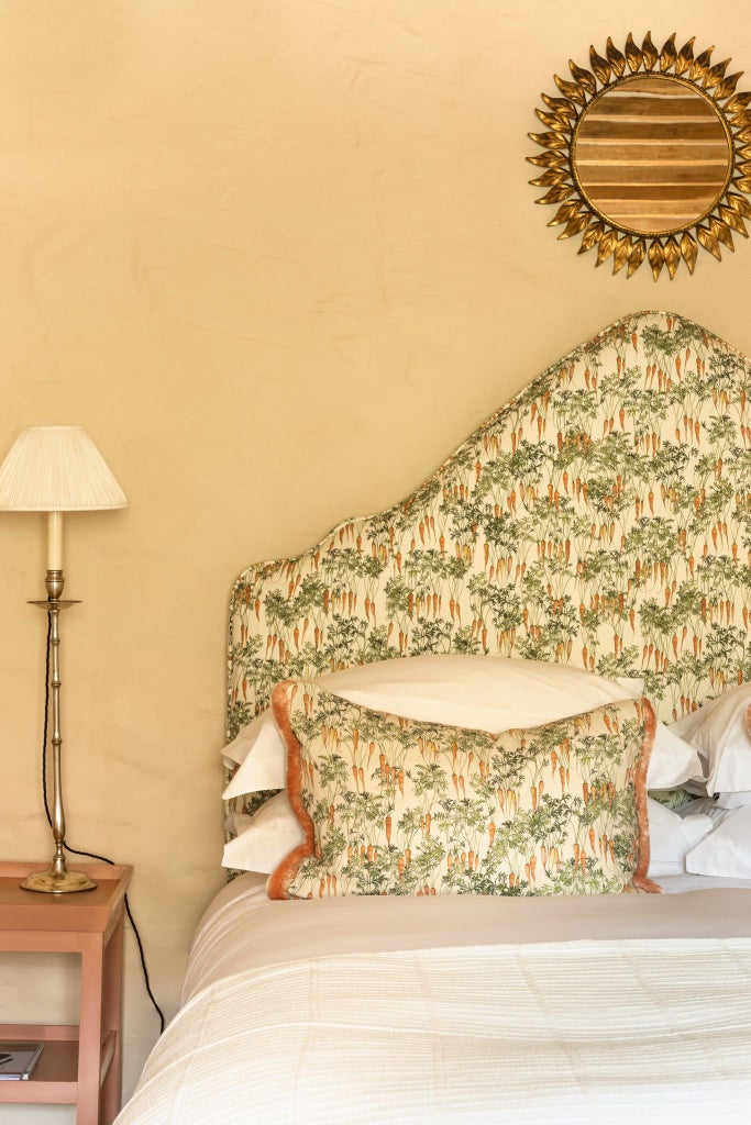 Rustic luxe garden cottage room with soft sage linens, antique wooden furnishings, and delicate botanical artwork against warm, textured stone walls