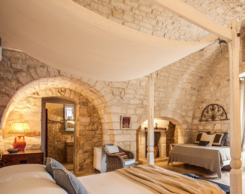 Rustic stone walls, elegant wooden furnishings, and a plush white bed in a luxurious Junior Suite at Masseria Cervarolo in Puglia, Italy