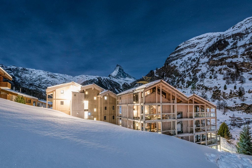 Modern luxury hotel with glass-walled rooms and infinity pool overlooking the Matterhorn mountain peak in Swiss Alps at sunset