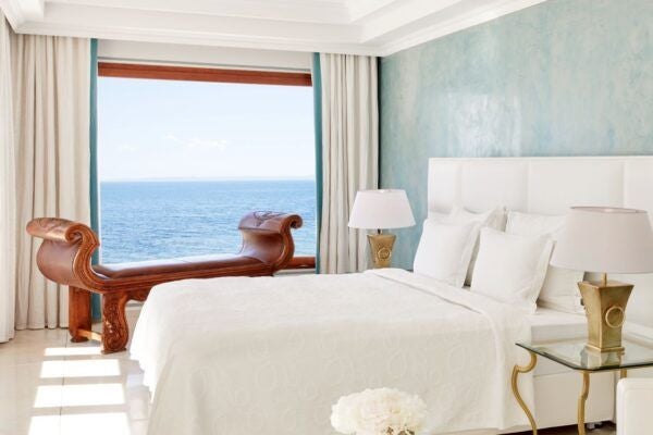 Luxurious two-bedroom suite at scenset Beach Resort, overlooking azure Aegean waters, featuring elegant white furnishings and expansive private balcony