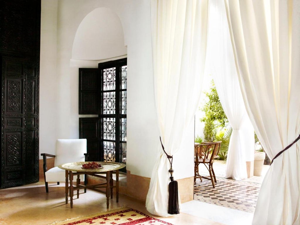 Traditional Moroccan riad with elegant white archways, serene courtyard garden, central fountain and luxurious poolside loungers in dappled sunlight