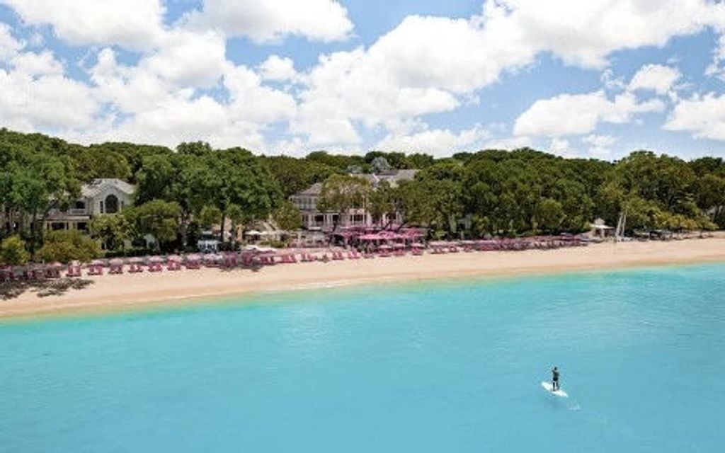 Pristine beachfront resort with white colonial-style buildings, swaying palm trees and turquoise Caribbean waters under a sunny sky