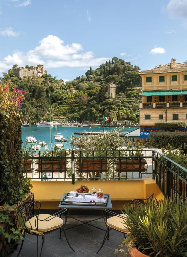 Elegant Mediterranean hotel with stone balconies overlooking turquoise coastline, featuring terra-cotta roof and cascading bougainvillea