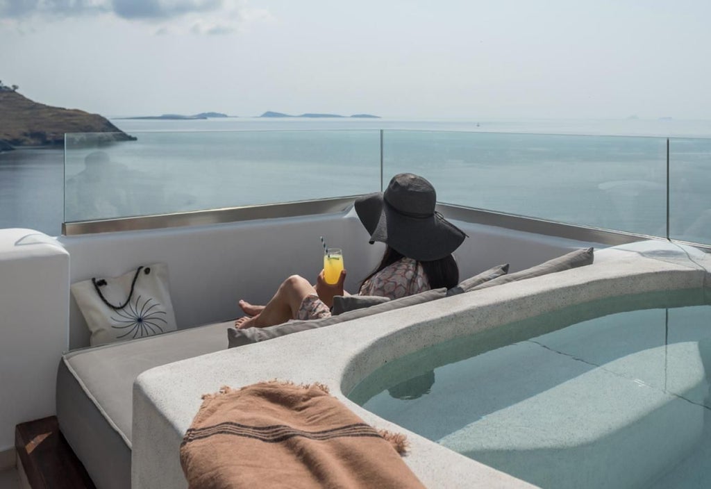 Elegant white-walled Grecian honeymoon suite with minimalist decor, sea-view balcony, plush king bed, and romantic sunset lighting in scenic coastal setting