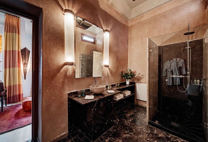 Traditional Moroccan riad courtyard with ornate archways, mosaic tilework, and elegant seating around a central fountain in warm evening light