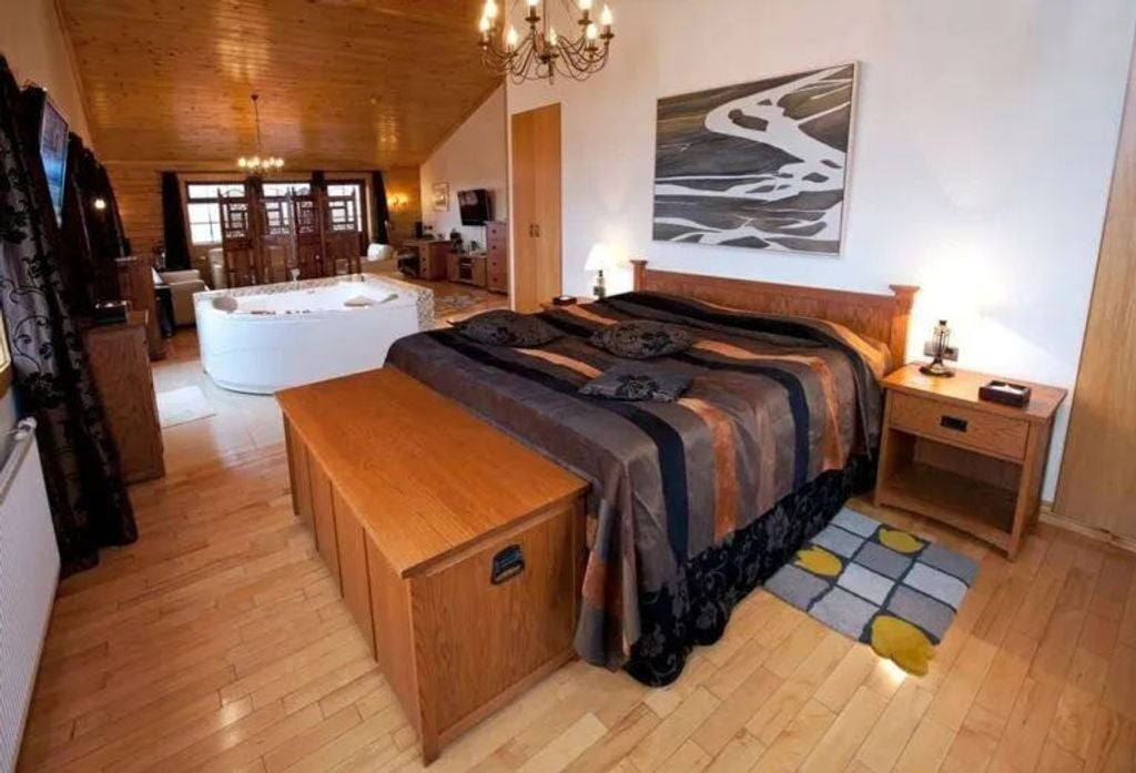 Spacious master suite with rustic wood accents, panoramic windows overlooking Icelandic landscape, plush king bed and seating area