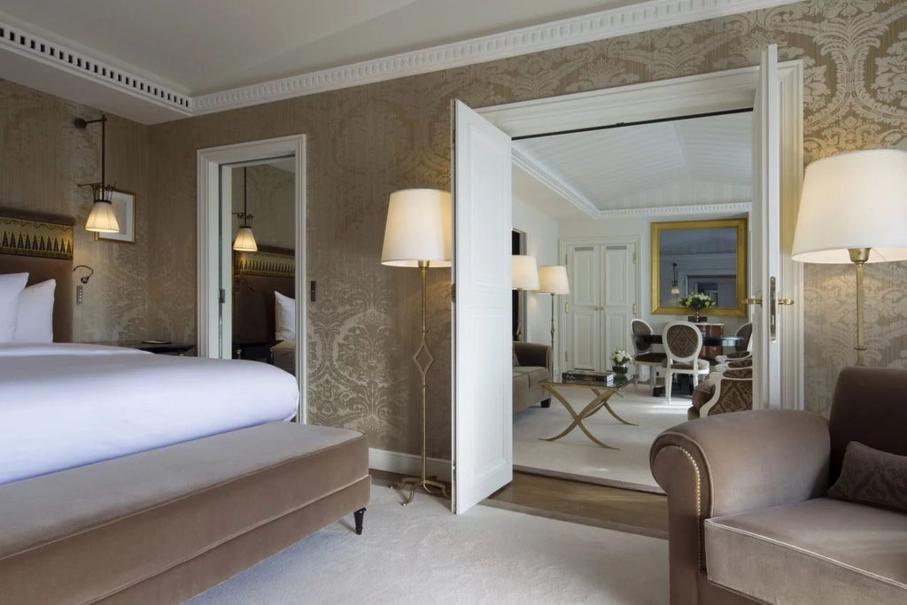 Elegant Parisian luxury suite with plush cream furnishings, sophisticated marble bathroom, and expansive city views through large windows at prestigious urban hotel