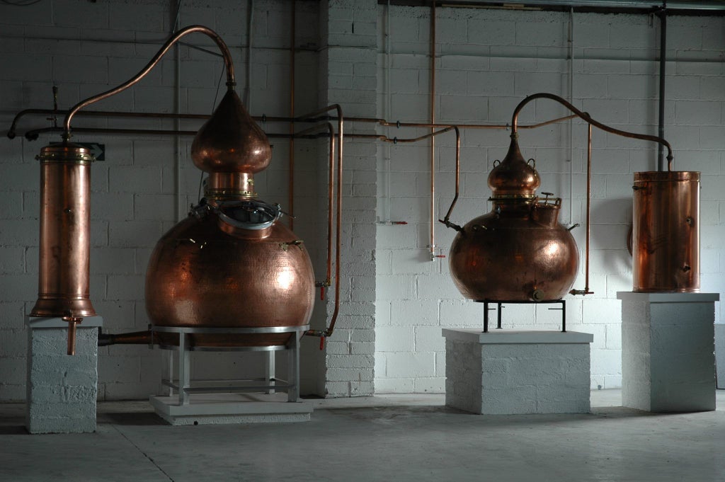 Elegant copper stills gleam in rustic stone-walled distillery, soft ambient light highlighting artisanal whiskey-making process in scenic Irish countryside