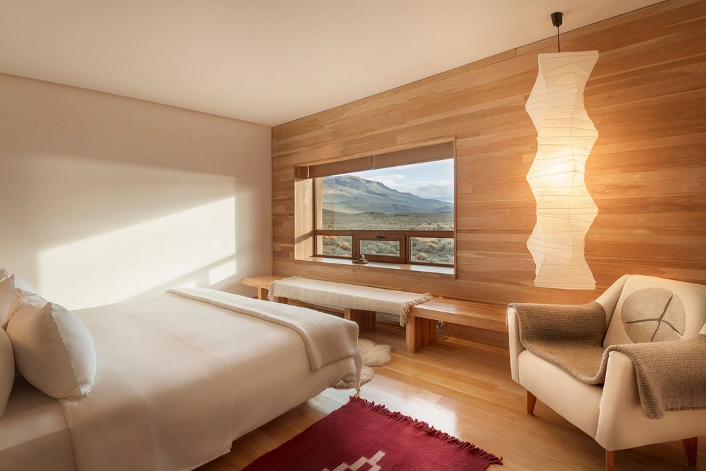 Modern minimalist luxury lodge with curved wooden facade nestled against rugged Patagonian landscape at sunset, Torres del Paine peaks beyond