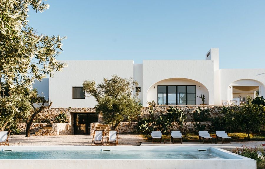 Minimalist white stone farmhouse nestled in Puglia's olive groves, featuring clean architectural lines and serene Mediterranean landscape at sunset