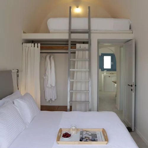 Elegant white-washed Greek villa bedroom with panoramic Aegean Sea view, traditional stone walls, and luxurious minimalist Mediterranean decor