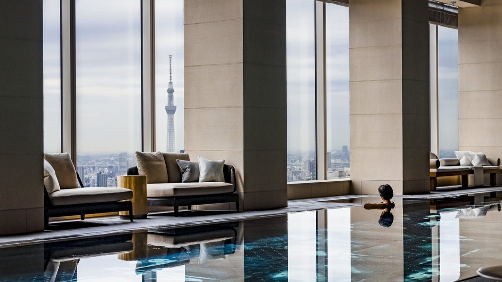 Modern luxury hotel lobby with soaring glass windows, sleek marble floors, gold accents, and panoramic views of Tokyo's skyline