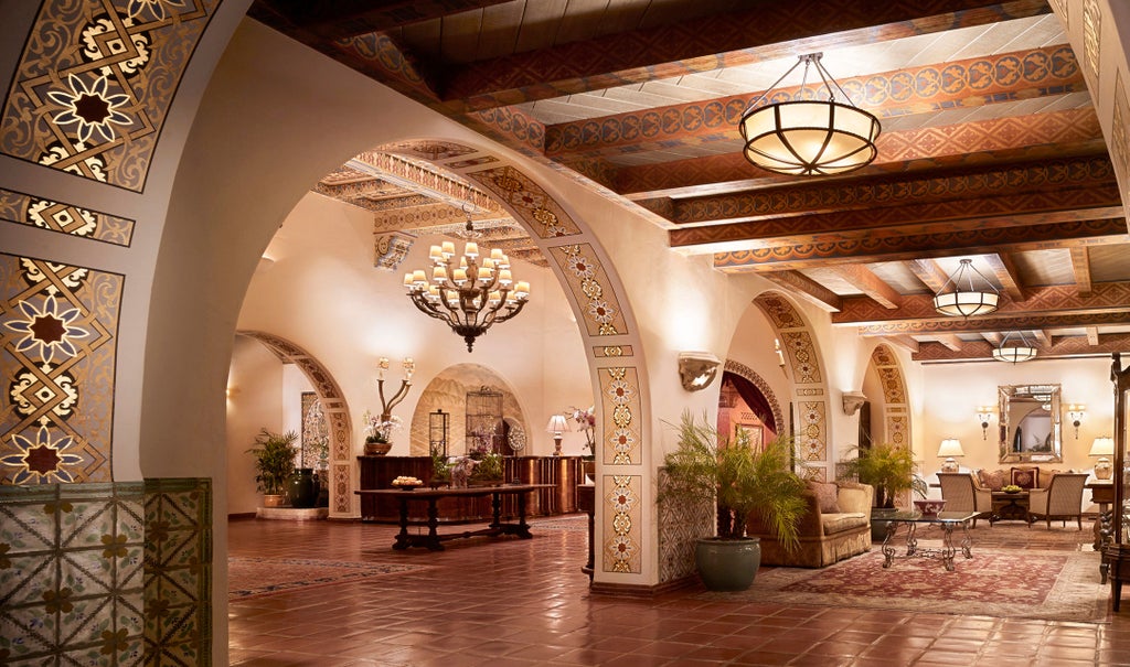 Mediterranean-style luxury beachfront hotel with white stucco walls, red tile roofs and lush palm gardens overlooking Pacific Ocean at sunset