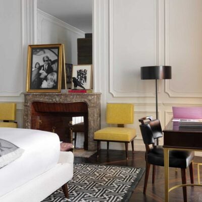 Elegant boutique hotel room with soft neutral tones, plush bedding, designer furniture, and panoramic windows overlooking Roman architecture at [Hotel] in Italy